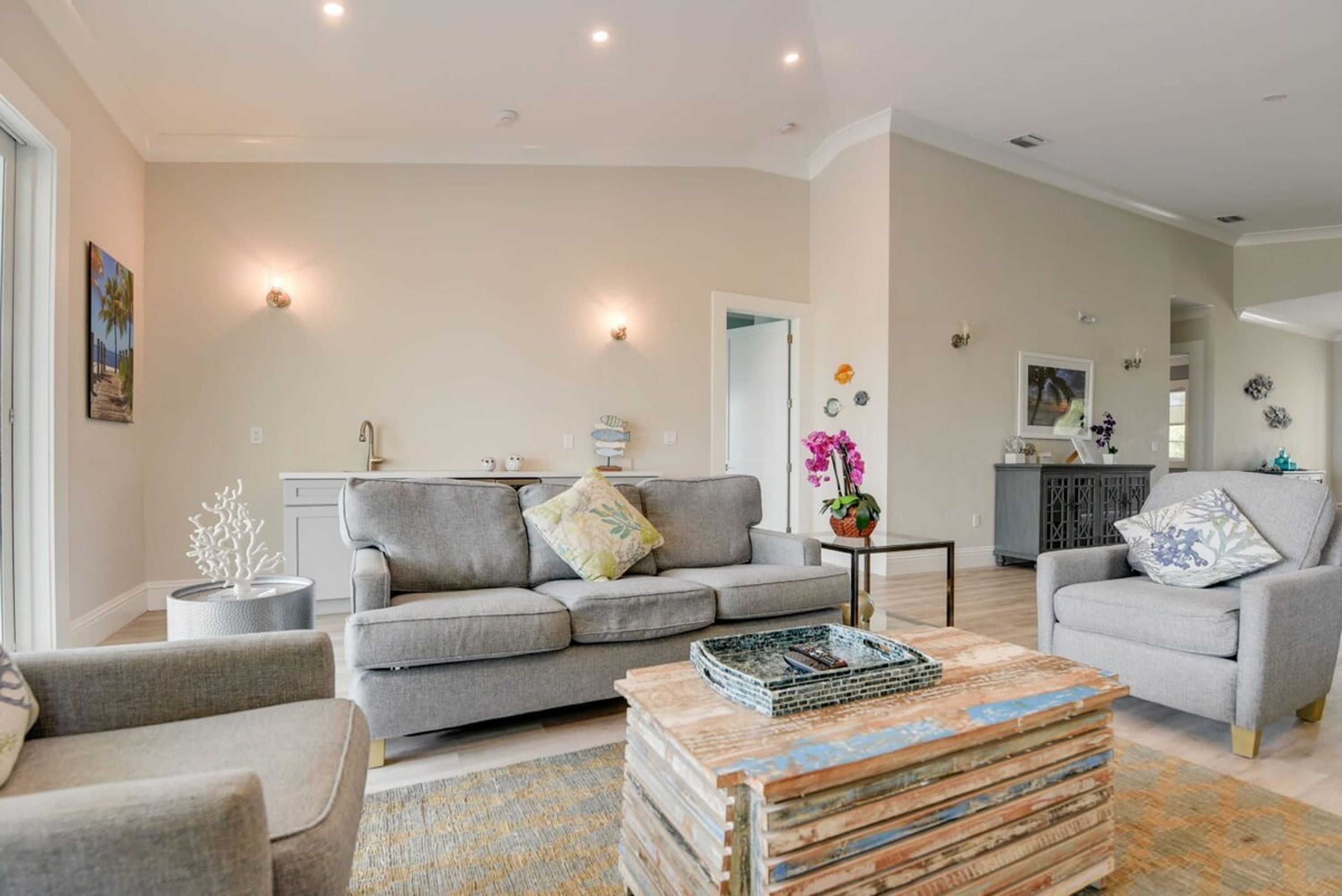 A spacious living room with a grey sofa, a coffee table, and a kitchen in the background.
