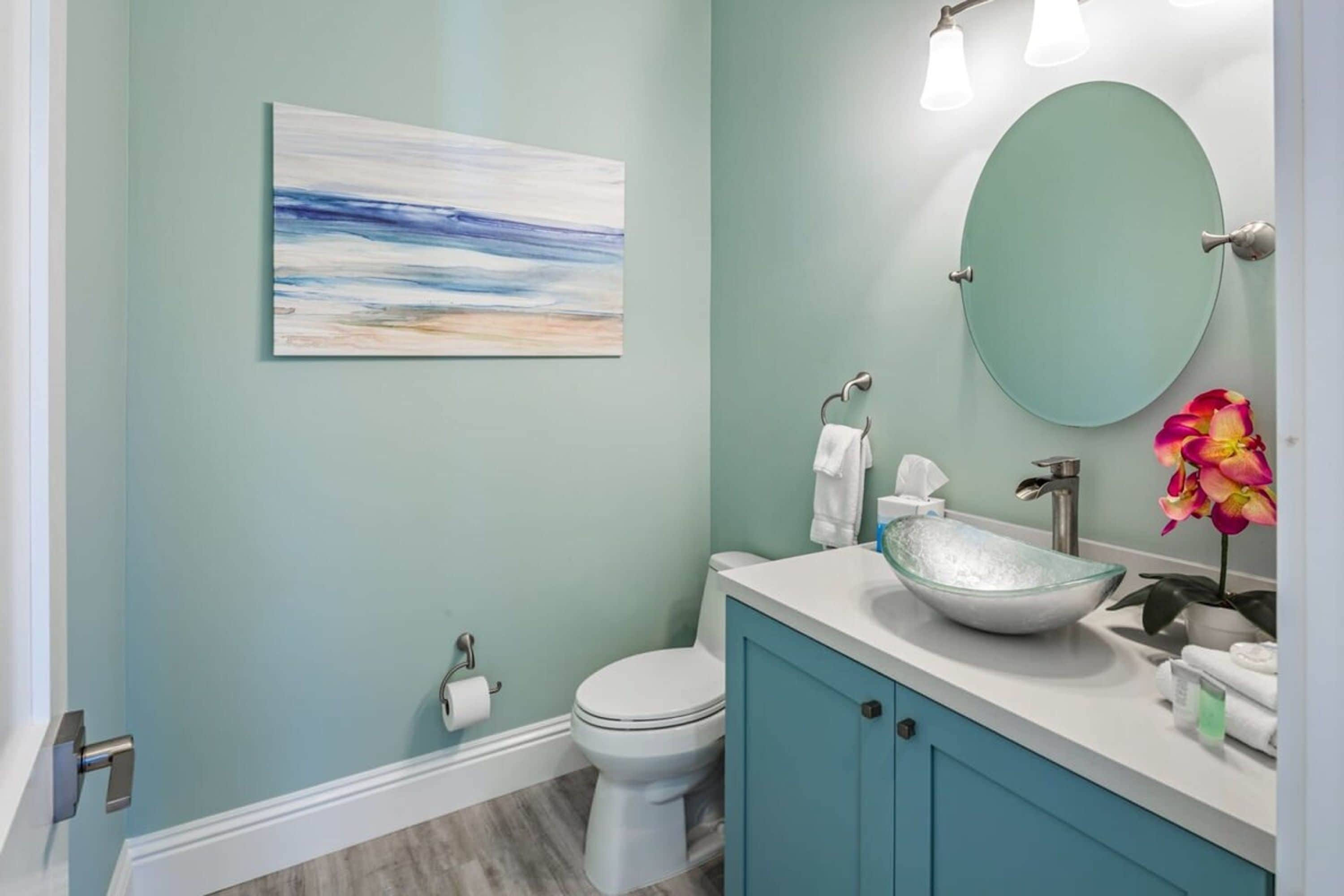 A bathroom with a white toilet, a glass sink, and a teal vanity.