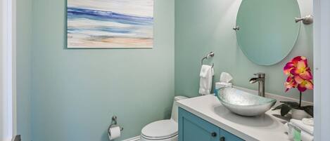 A bathroom with a white toilet, a glass sink, and a teal vanity.