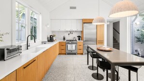 Una cucina moderna con mobili bianchi, un frigorifero in acciaio inossidabile, un piano di lavoro in legno e un'area pranzo con tavolo e sedie.