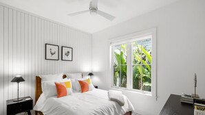Camera da letto con un letto, due comodini, una scrivania, una sedia, una ventola a soffitto e una finestra vista verde.