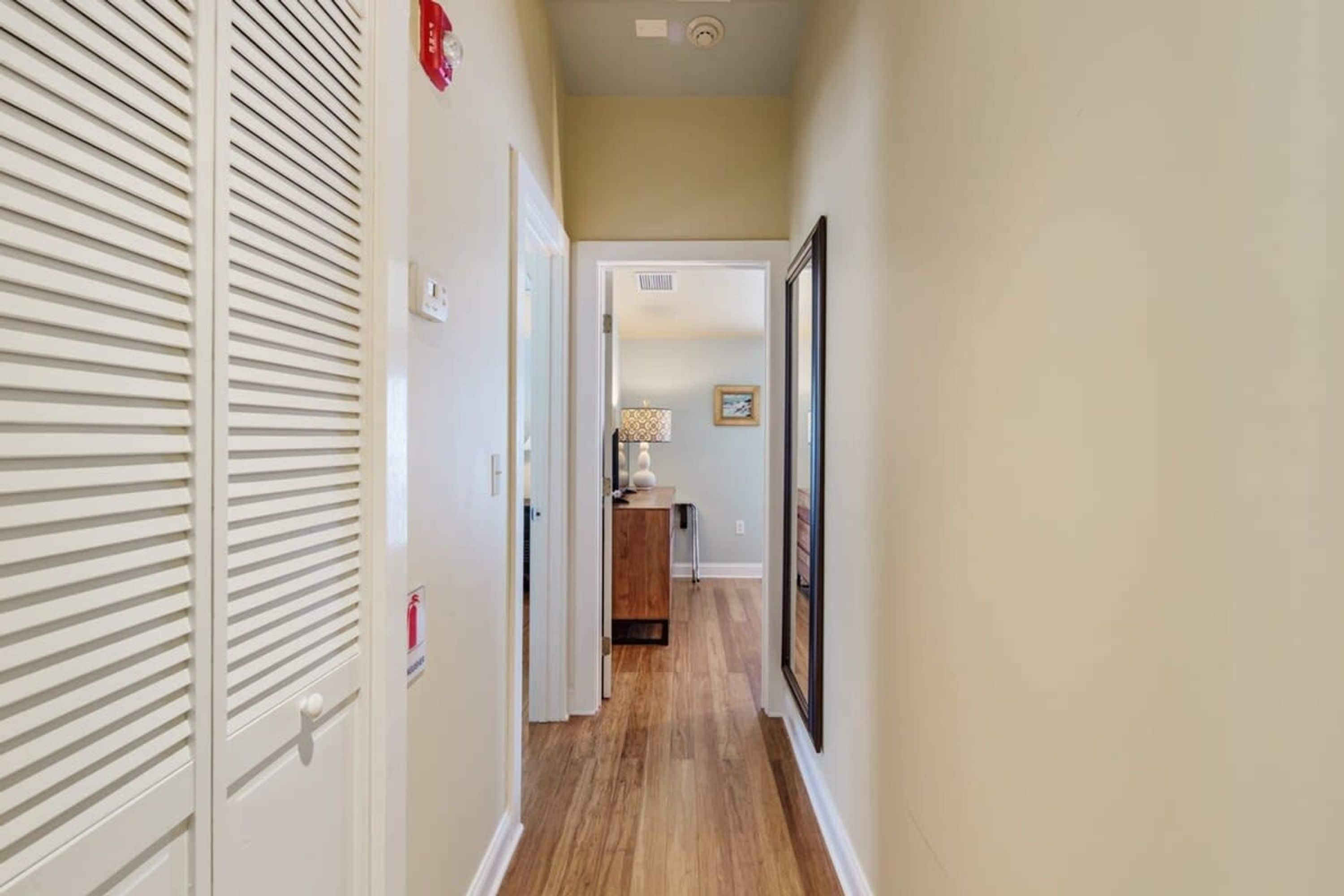 A narrow hallway with wooden flooring, white walls, and a door with horizontal slats.