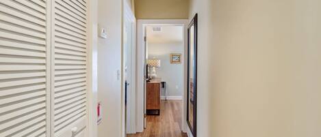 A narrow hallway with wooden flooring, white walls, and a door with horizontal slats.