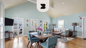 Un salon spacieux avec un plafond haut, un plancher en bois, une table à manger avec des chaises, un canapé et un téléviseur.