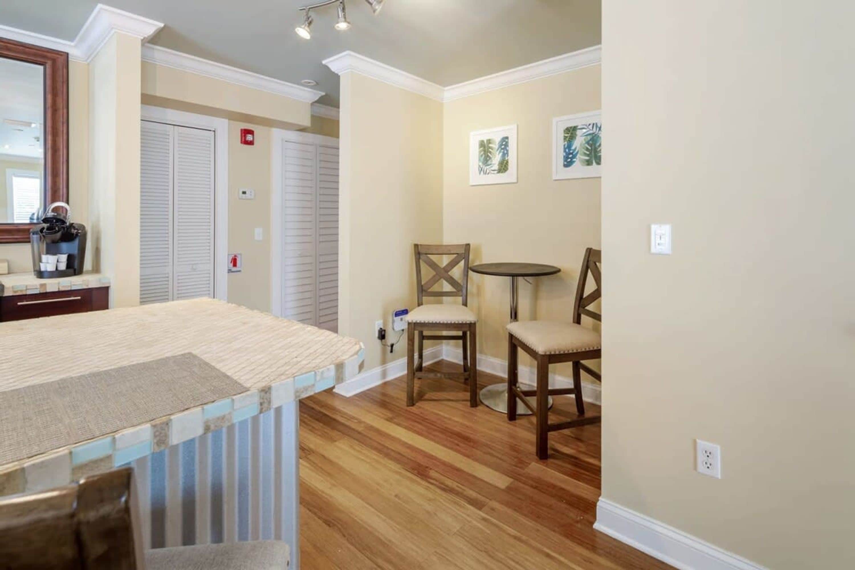 A room with a wooden floor, a kitchen area with a countertop, a dining table with chairs, and a door with a closet.