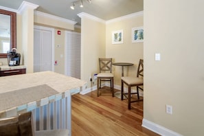 A room with a wooden floor, a kitchen area with a countertop, a dining table with chairs, and a door with a closet. - Sky Suites Retreat by Brightwild 2 Stunning Condos (Key West)