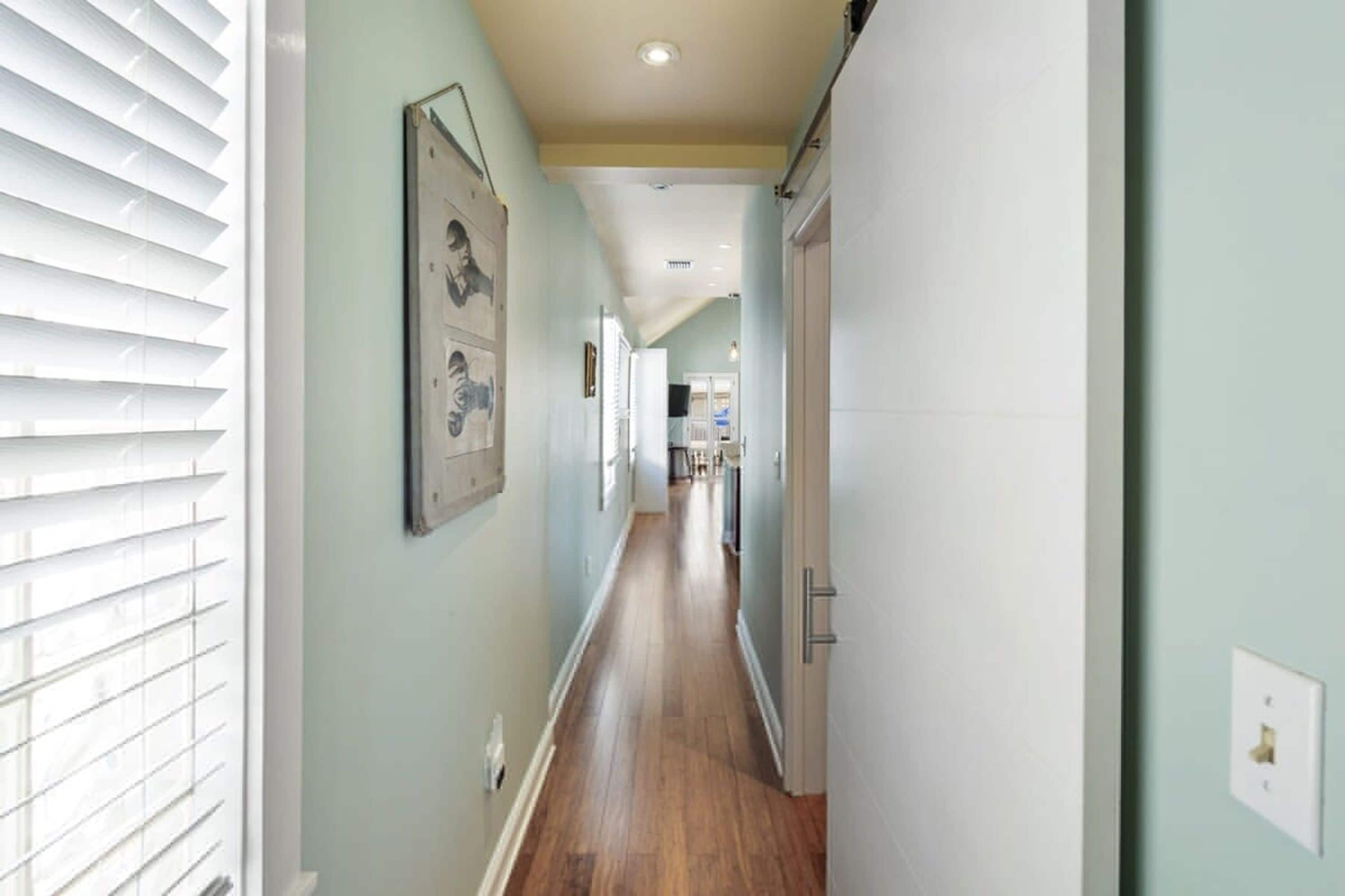 A narrow hallway with wooden flooring, light green walls, and a ceiling light.