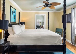 Ein Hotelzimmer mit Himmelbett, Deckenventilator, einem gerahmten Bild an der Wand und Blick auf den Flur.