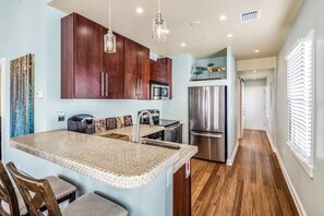 A modern kitchen with dark wood cabinets, a stainless steel refrigerator, and a patterned island with bar stools. - Sky Suites Retreat by Brightwild 2 Stunning Condos (Key West)