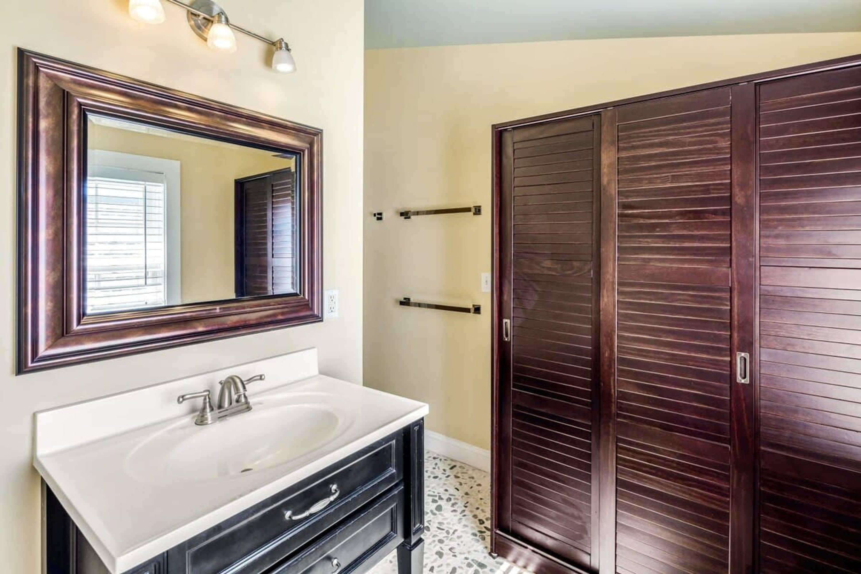 A bathroom with a large mirror, a white sink, and a dark wooden wardrobe.