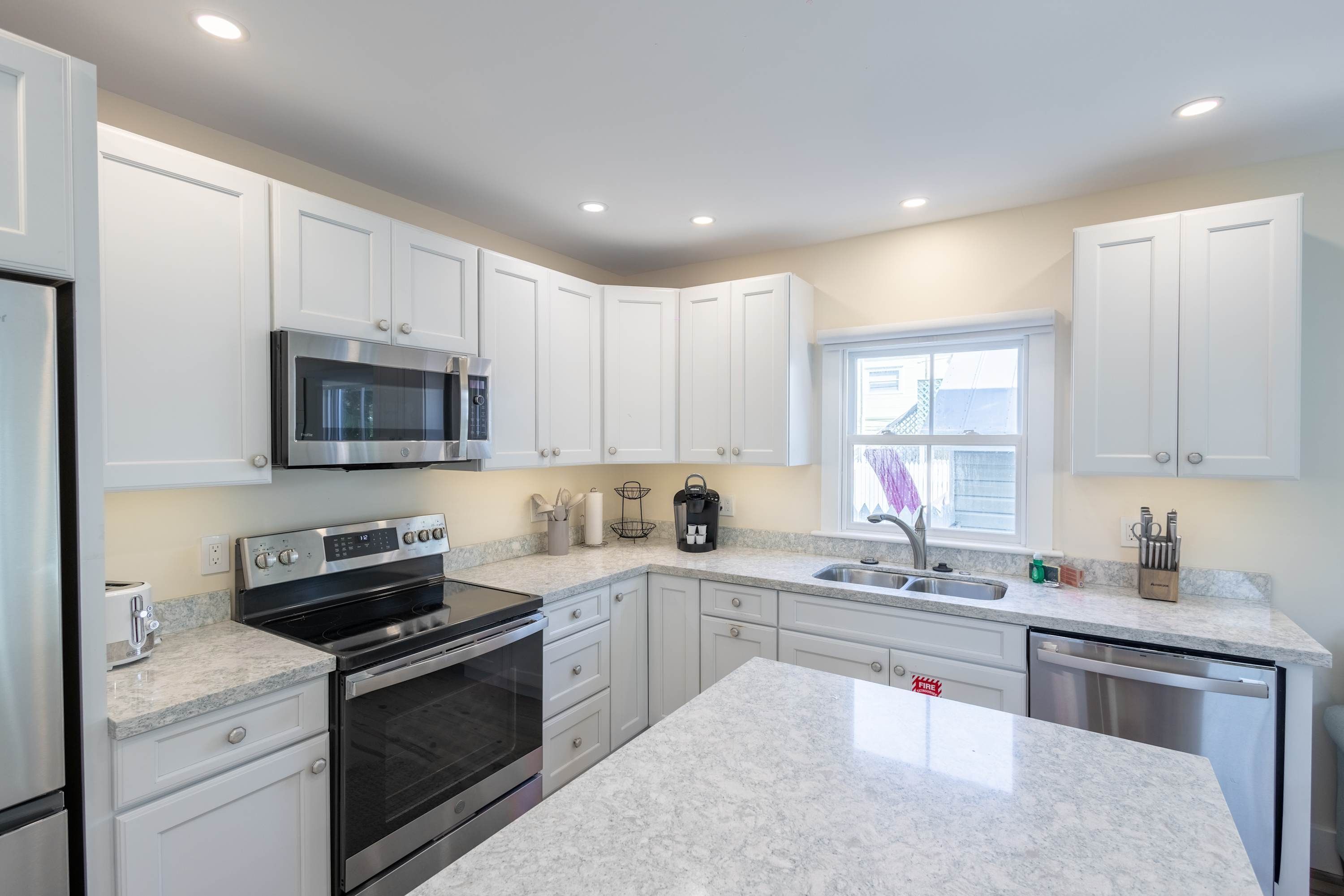 A modern kitchen with white cabinets, a stainless steel microwave, a built-in oven, a dishwasher, and granite countertops.
