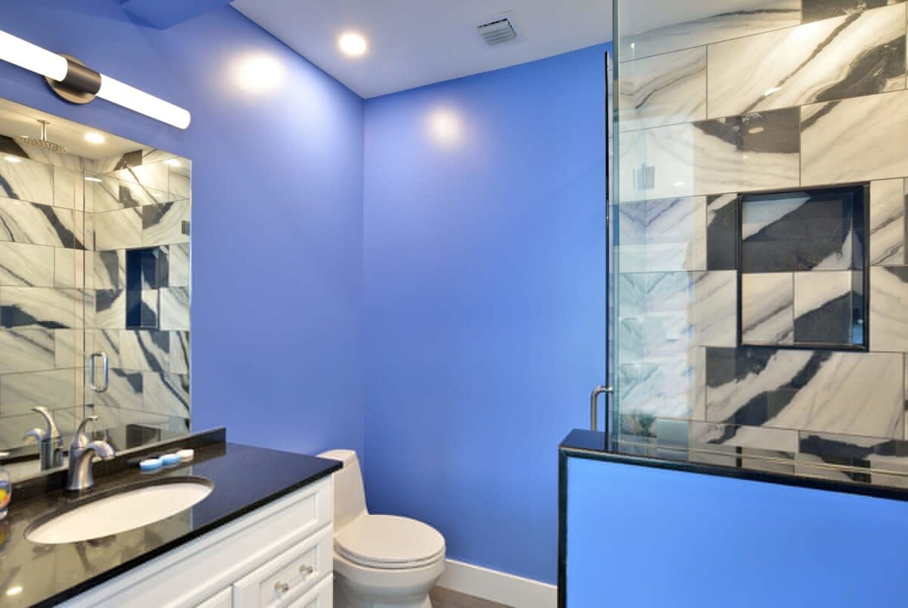 A modern bathroom with a blue wall, a marble backsplash, and a glass shower enclosure.