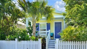 Een huis met een witte picket fence, een blauwe deur en een veranda met een stoel.
