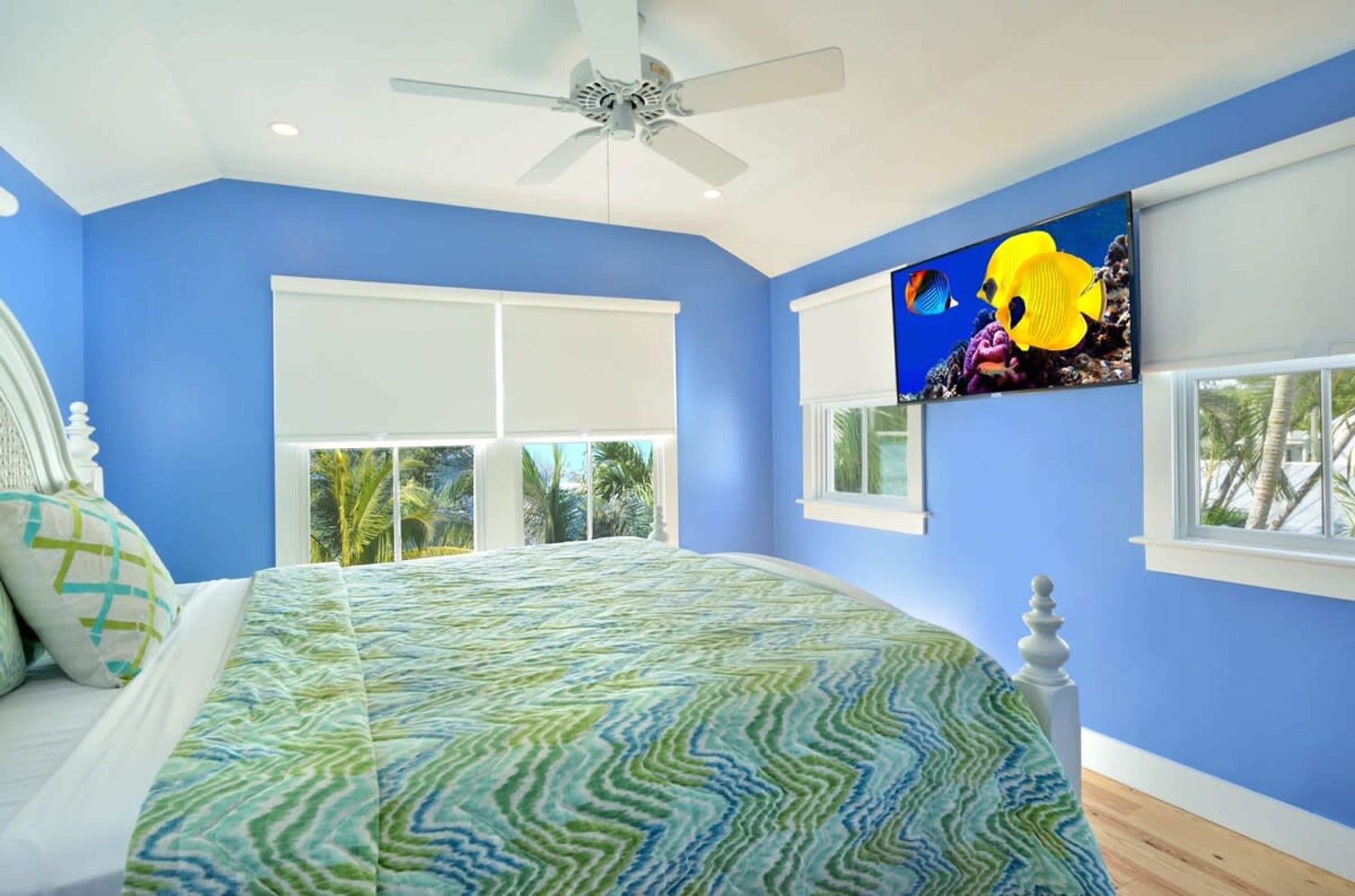 Een slaapkamer met een bed, een plafondventilator, een groot raam en een tv aan de muur.