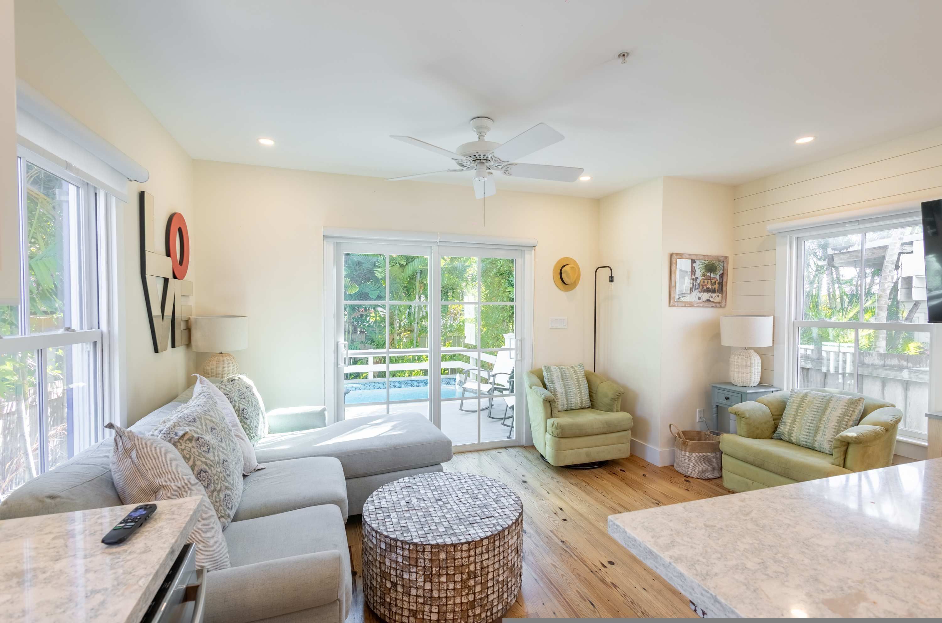 A spacious living room with a large window, a ceiling fan, a sofa, a round coffee table, and a TV.