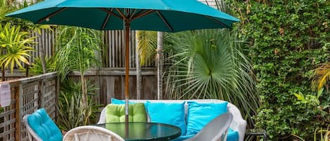 An outdoor patio with wicker furniture, a round glass table, and a teal umbrella.
