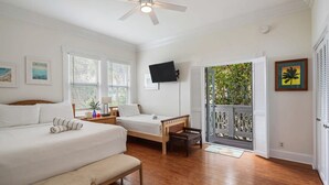 A bedroom with two beds, a ceiling fan, a TV, and a balcony with a view of greenery. - Sunnyside Up by Brightwild Pool Parking (Key West)