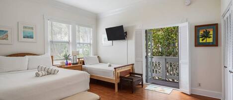 Un dormitorio con dos camas, ventilador de techo, televisor y balcón con vistas a zonas verdes.