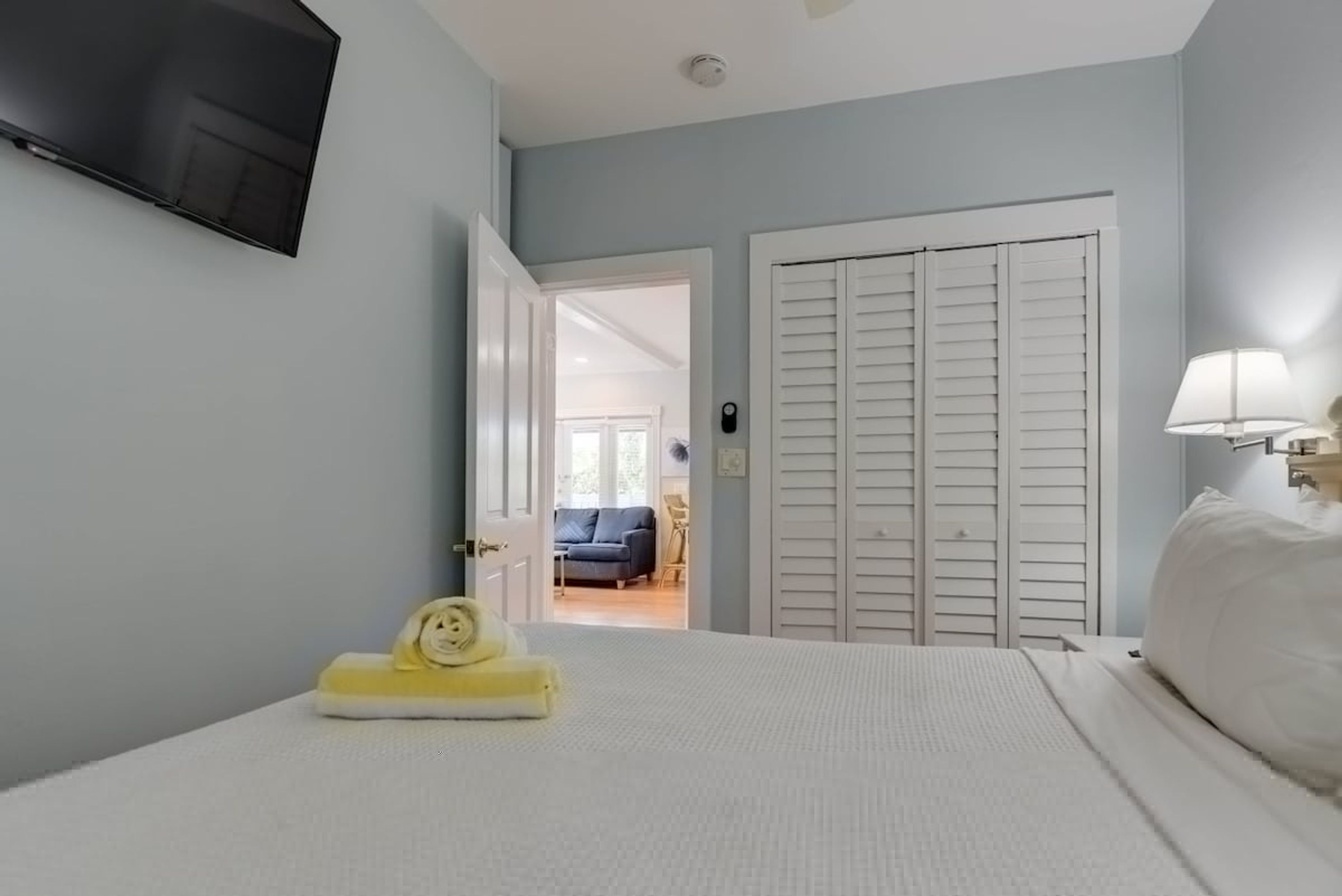 Una camera da letto con un letto, una TV a parete, una porta che dà su un'altra stanza e una lampada sul comodino.