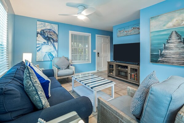 A living room with a blue sofa, a coffee table, a TV, and artwork on the walls. - Road s End by Brightwild Steps to Duval St (Key West)