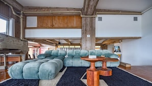 Un salon moderne avec un canapé d’angle, des poutres en bois et un tapis noir.