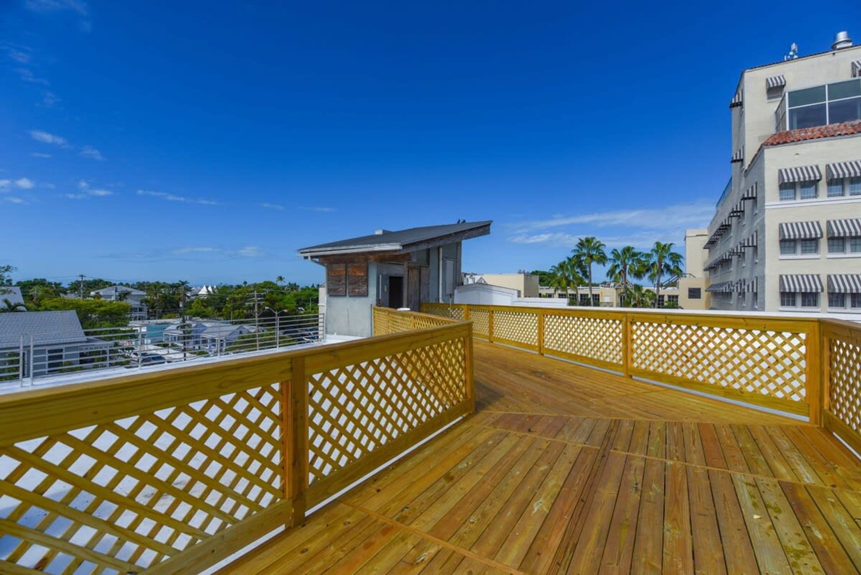 A wooden deck with a lattice railing, overlooking a residential area with houses and palm trees.