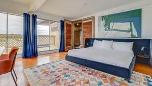 Une chambre avec un grand lit, une vue sur l’extérieur grâce à une porte-fenêtre coulissante et un tapis coloré.