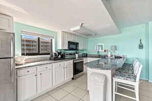 A modern kitchen with white cabinets, a granite countertop, and a central island with seating. - Oceanfront Penthouse Pool Hot Tub Beach Access (Daytona Beach Shores)