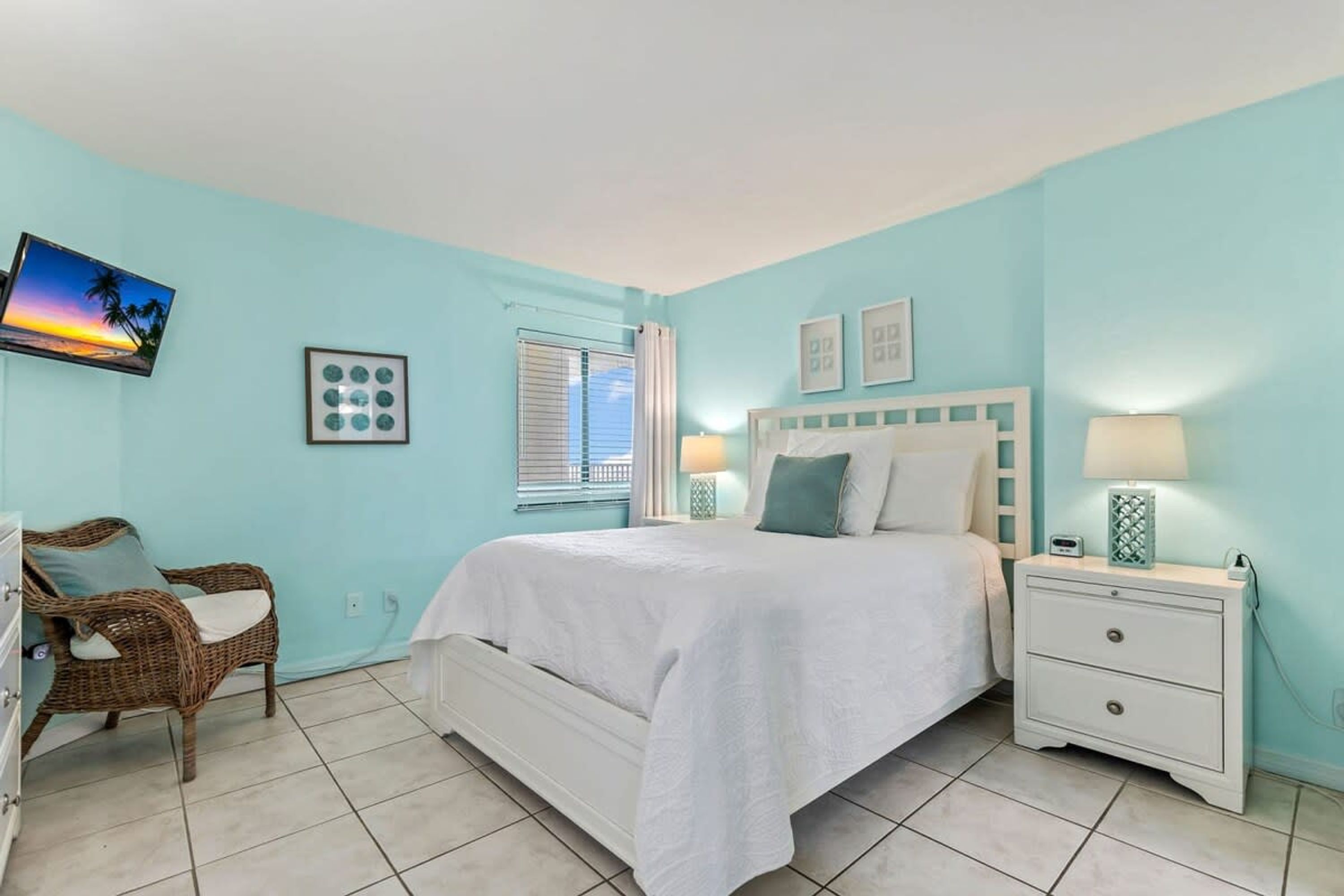 A bedroom with a bed, a nightstand, a chair, and a wall-mounted TV.