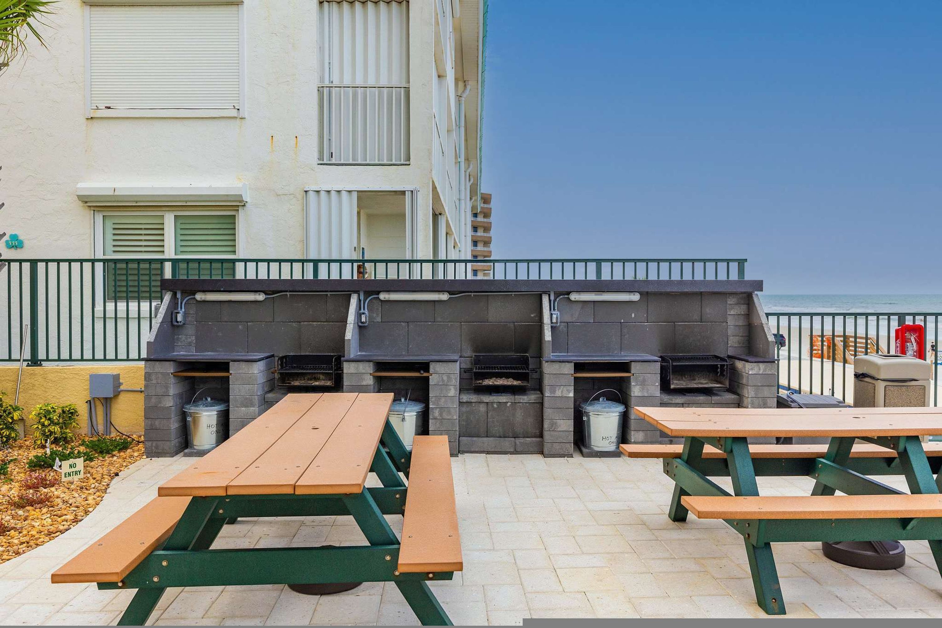 An outdoor patio area with picnic tables and a barbecue grill setup against a building facade.