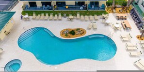 A large, irregularly shaped swimming pool with lounge chairs and tables around it, and a building with balconies in the background. - Oceanfront Penthouse Pool Hot Tub Beach Access (Daytona Beach Shores)