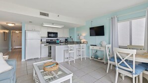 Un espacio habitable compacto con kitchenette, comedor y televisor montado en la pared.