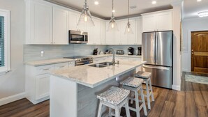 A modern kitchen with white cabinets, stainless steel appliances, and a large island with bar stools. - Southernmost View by Brightwild Pool H20 Views (Key West)