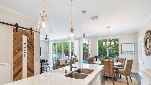 A kitchen with a large island, two pendant lights, and a dining area with wicker chairs and a round table. - Southernmost View by Brightwild Pool H20 Views (Key West)