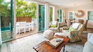 A spacious living area with a sliding glass door leading to a patio, furnished with a sofa, chairs, and a coffee table. - Southernmost View by Brightwild Pool H20 Views (Key West)