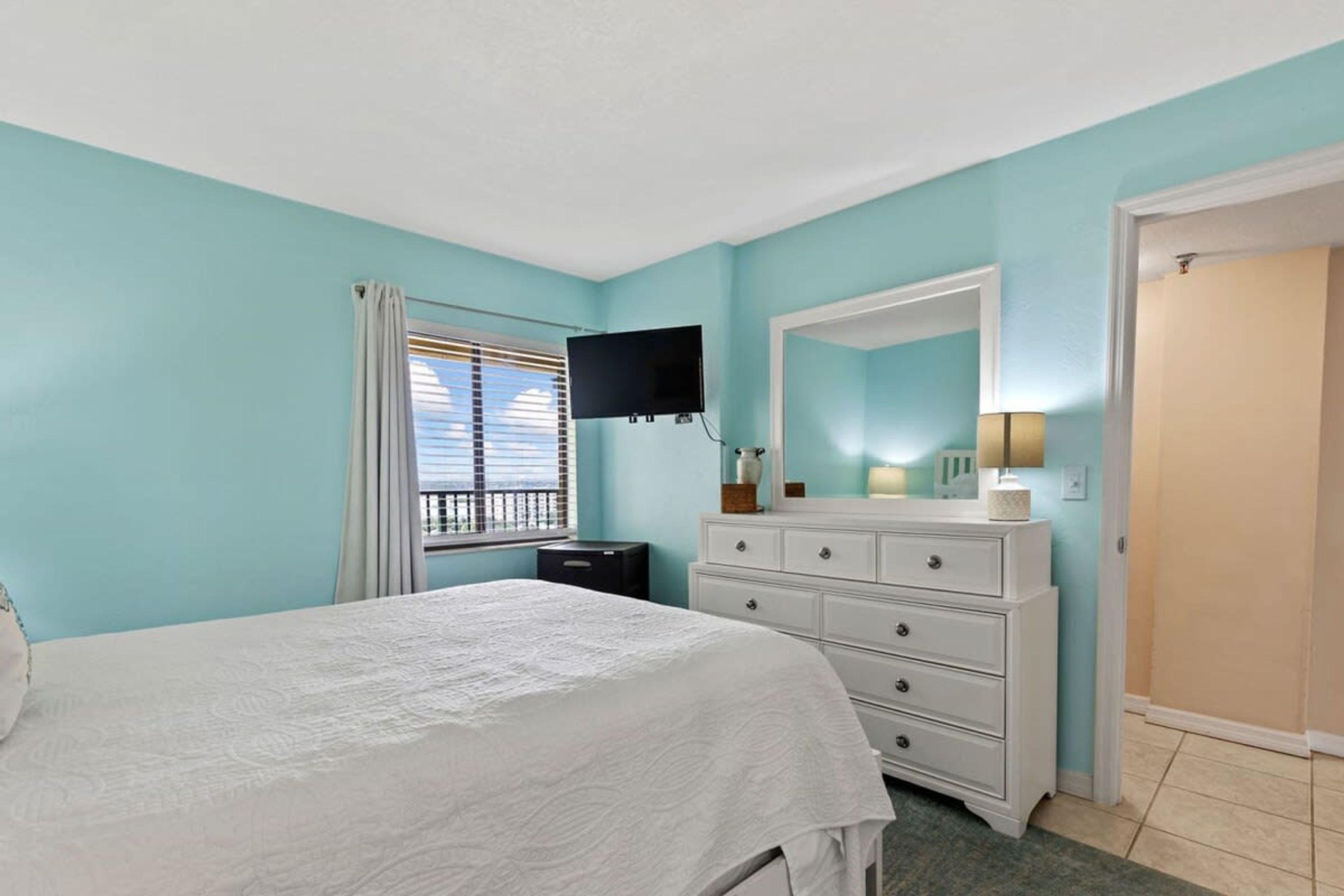 A bedroom with a bed, a dresser, a television, and a window with blinds.