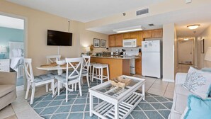 Un espacio habitable compacto con comedor, kitchenette y televisor montado en la pared.