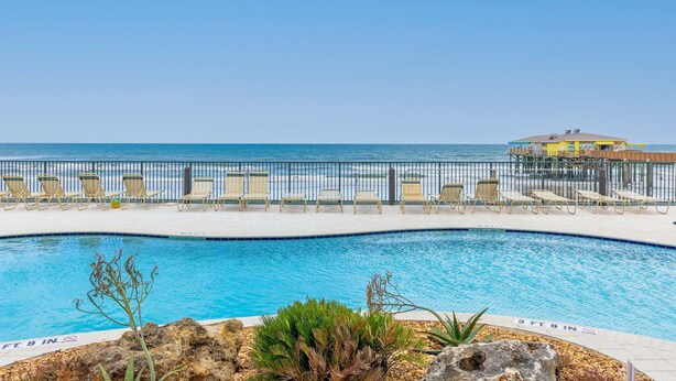 A swimming pool with lounge chairs and a view of the ocean. - Updated Ocean Front Condo Aquamarine Suite 201 (Daytona Beach Shores)