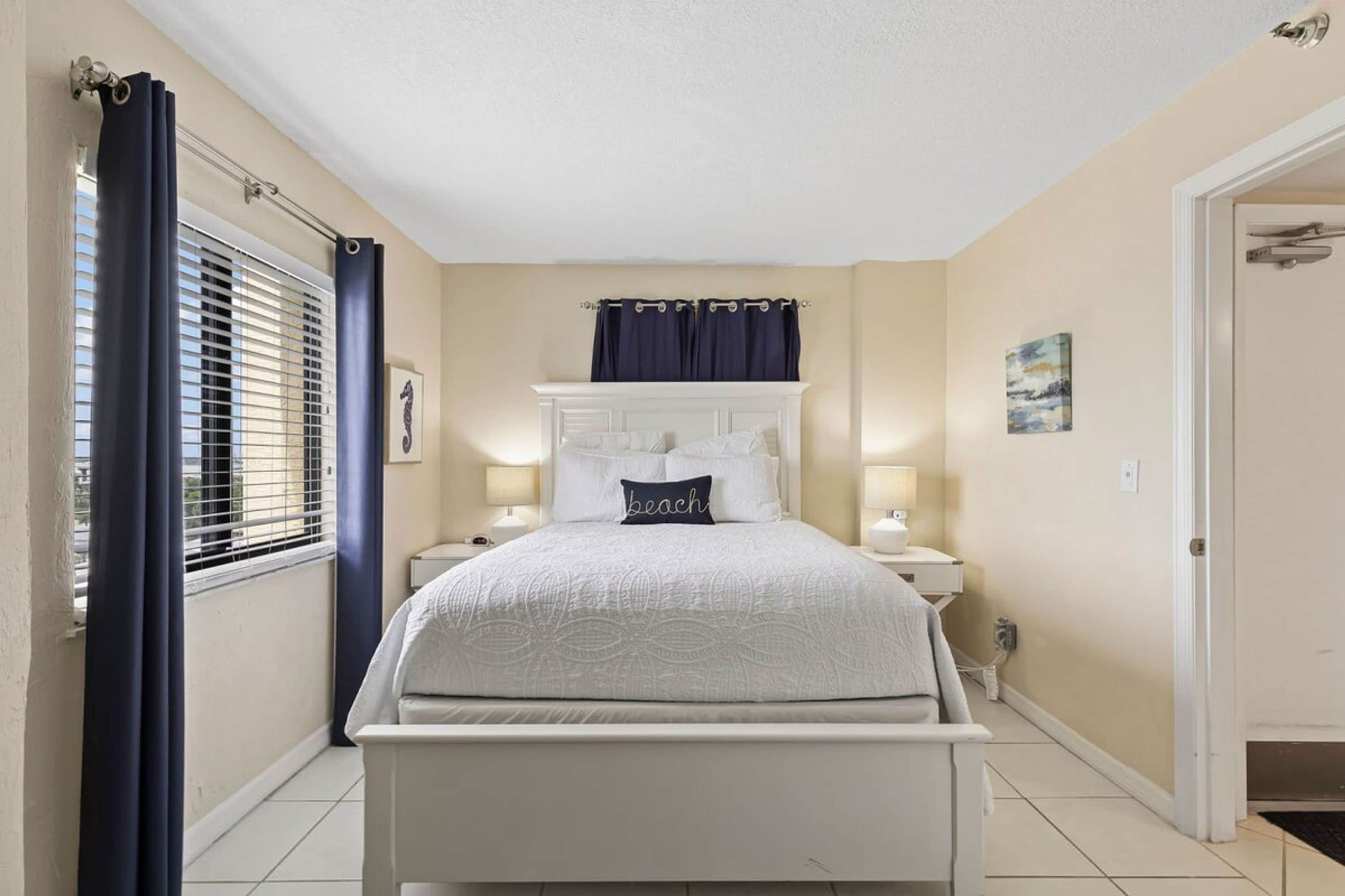 A bedroom with a bed, bedside tables, a window with curtains, and a door.