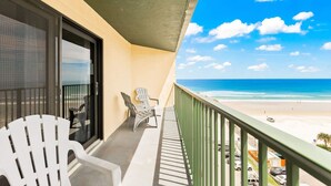A balcony with two white Adirondack chairs, a glass door, and a view of the beach. - Ocean Views Pool Hot Tub Seahorse Suite 907 (Daytona Beach Shores)