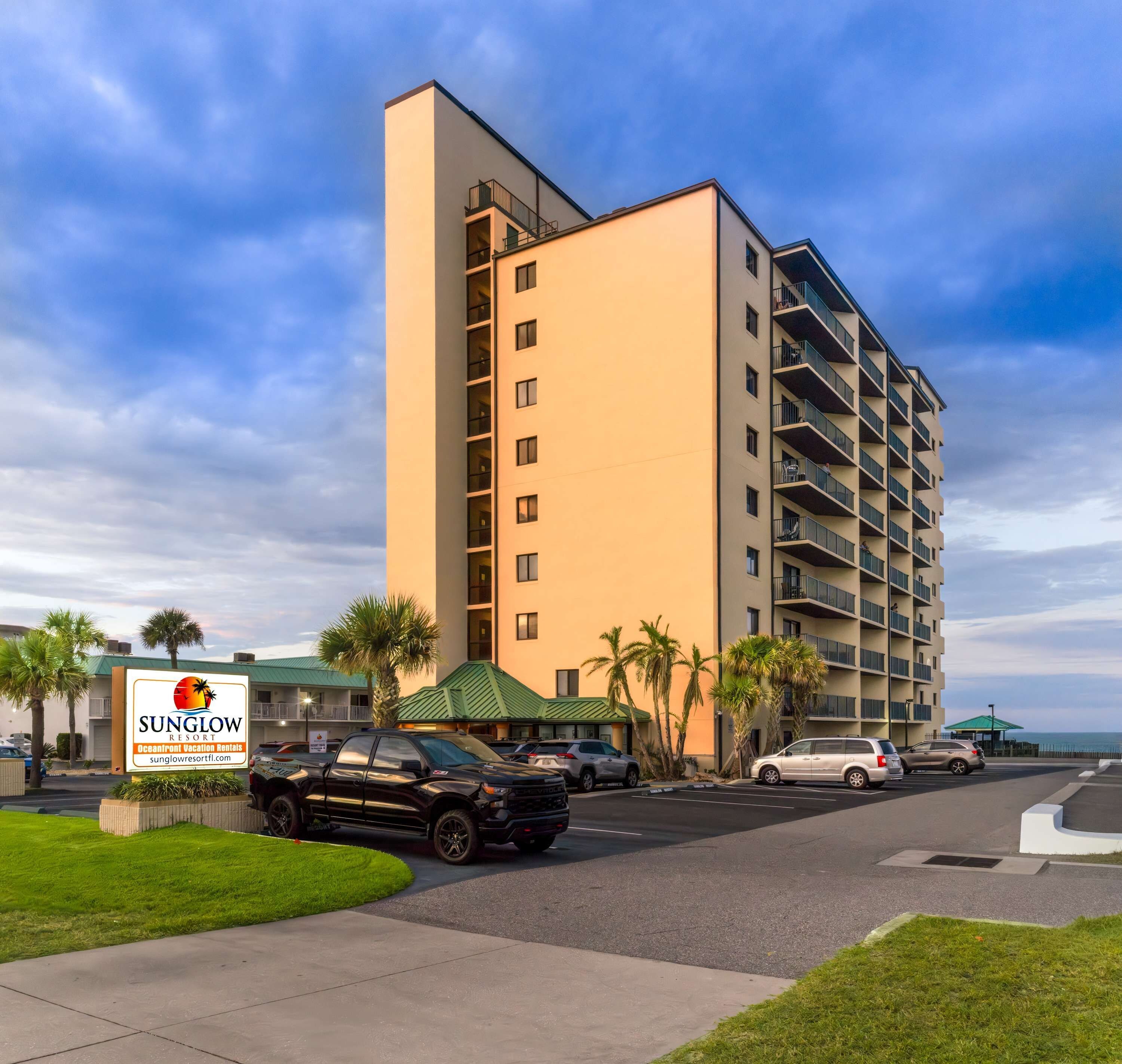 A multi-story hotel with a flat facade, a parking lot, and a sign indicating it is a vacation rental.