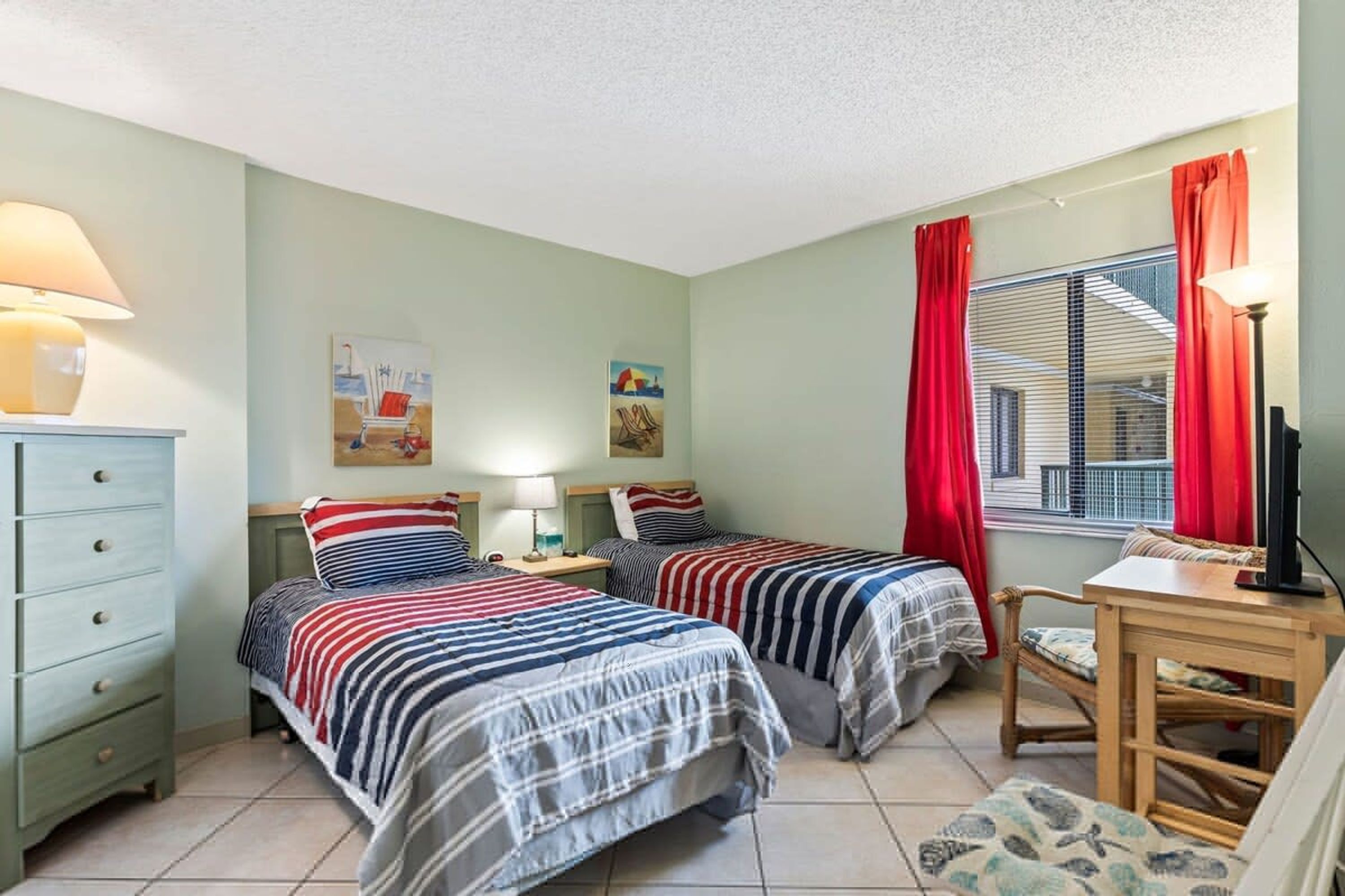 Una habitación con dos camas, un escritorio, una silla, un aparador y una ventana con cortinas.