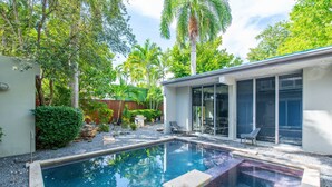 Et moderne hus med swimmingpool, omgivet af frodig vegetation og palmer.