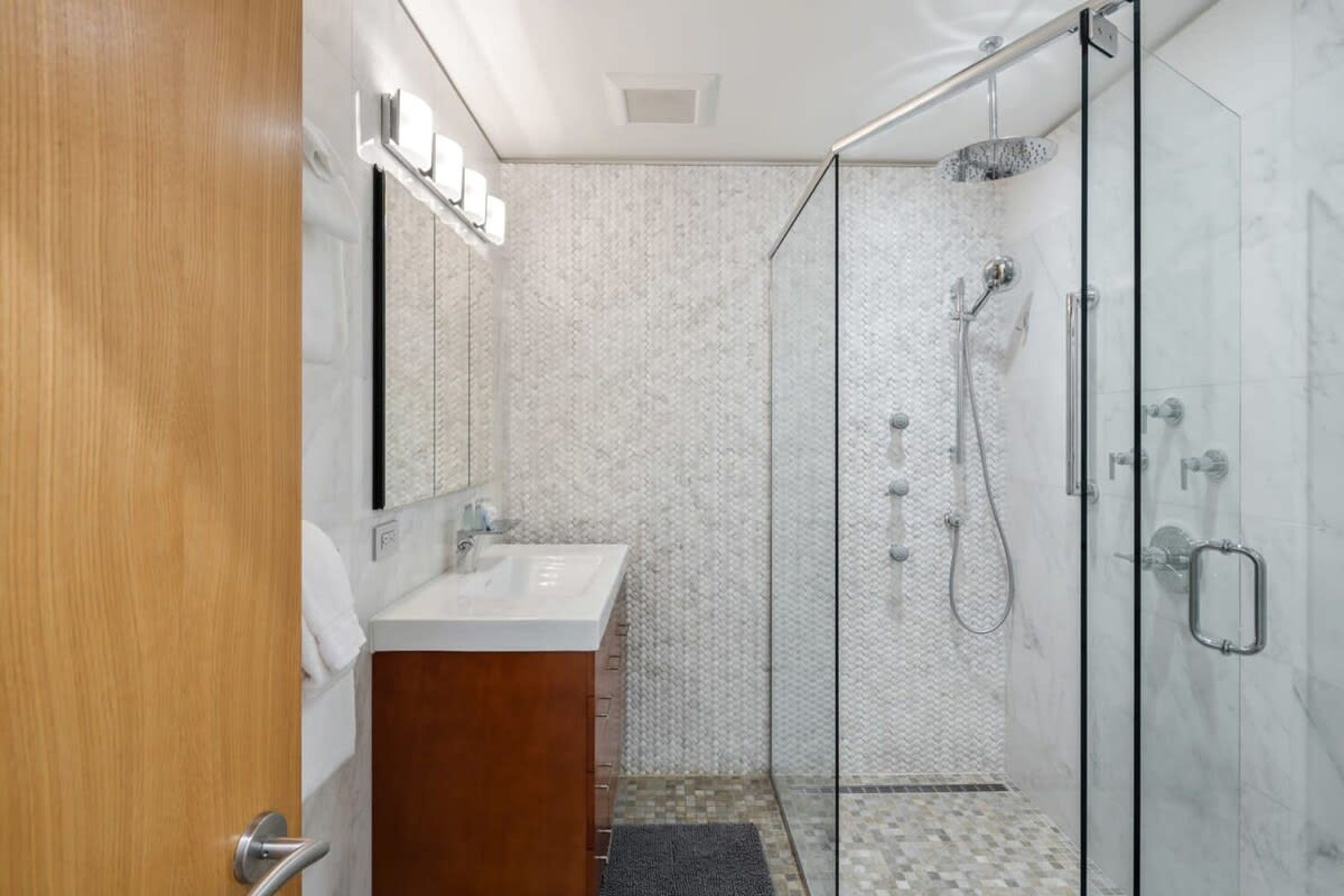 A modern bathroom with a glass shower enclosure, a wooden vanity, and a tiled shower floor.