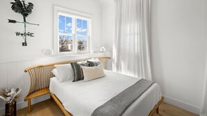 A bedroom with a wooden bed, white bedding, a window with white curtains, and a wall-mounted rooster compass. - Casa Romeo Gorgeous Ybor Apt Steps to 7th Ave (Tampa)