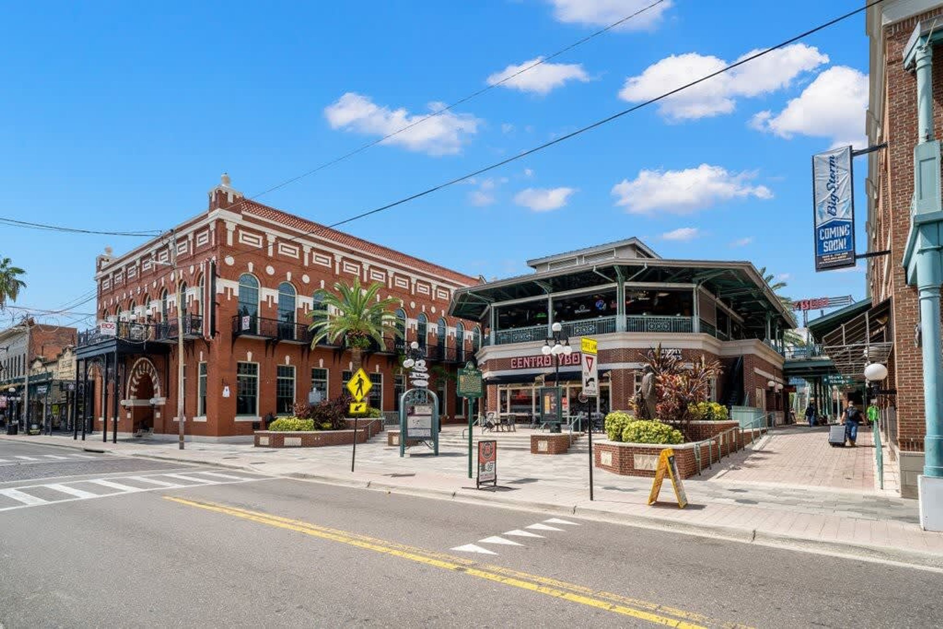 A street view with a historic building and a modern structure with a sign indicating a new business opening.