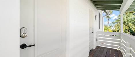 A white door with a keypad lock, a wooden deck, and a white railing.