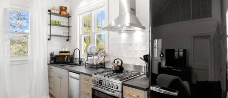 Una cocina moderna con estufa de acero inoxidable, refrigerador negro y ventana con vista a palmeras.