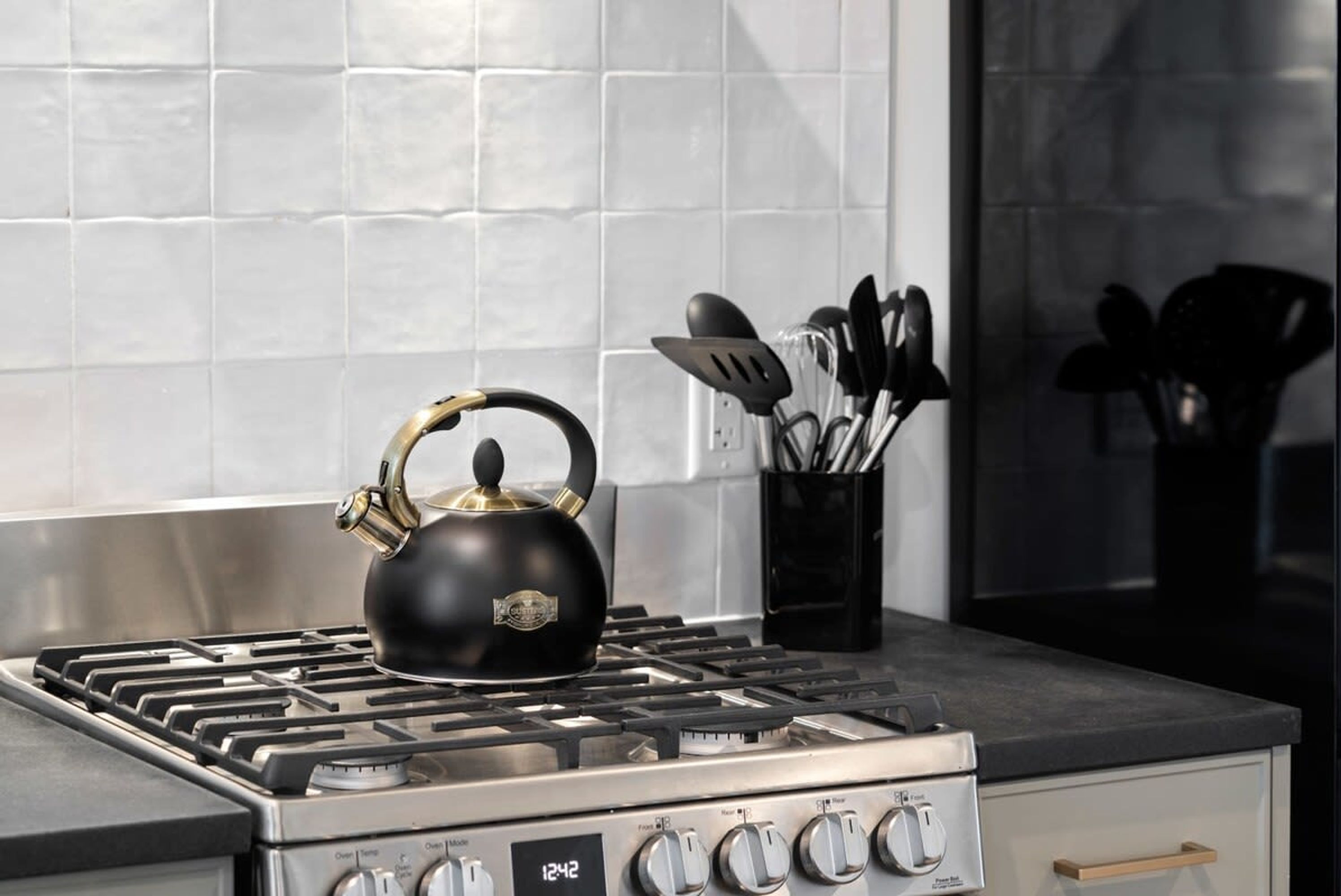 Una cocina con estufa a gas, un hervidor negro y un organizador de utensilios.