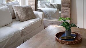 Ein Zimmer mit einem weißen Sofa, einem Couchtisch aus Holz mit einer Pflanze und einem großen Spiegel an der Wand.
